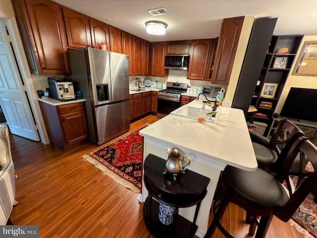 kitchen featuring sink, stainless steel appliances, a kitchen breakfast bar, backsplash, and hardwood / wood-style flooring