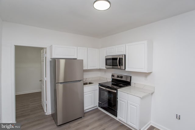 kitchen featuring light stone counters, white cabinetry, stainless steel appliances, and light hardwood / wood-style flooring