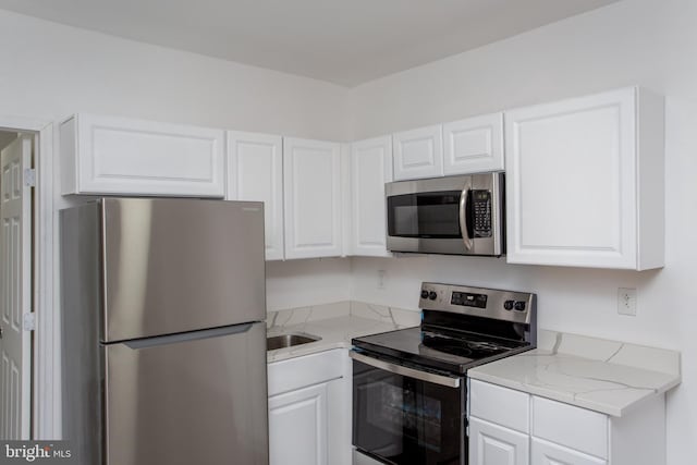 kitchen with light stone countertops, appliances with stainless steel finishes, white cabinetry, and sink