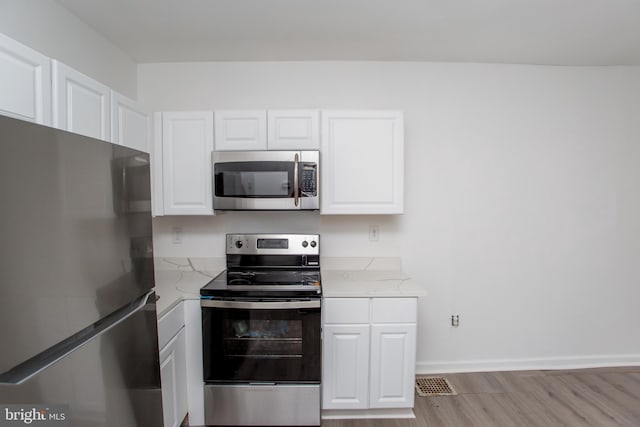 kitchen with light stone countertops, white cabinetry, stainless steel appliances, and light wood-type flooring