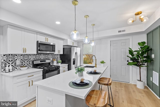 kitchen featuring a kitchen bar, appliances with stainless steel finishes, a kitchen island with sink, pendant lighting, and white cabinets