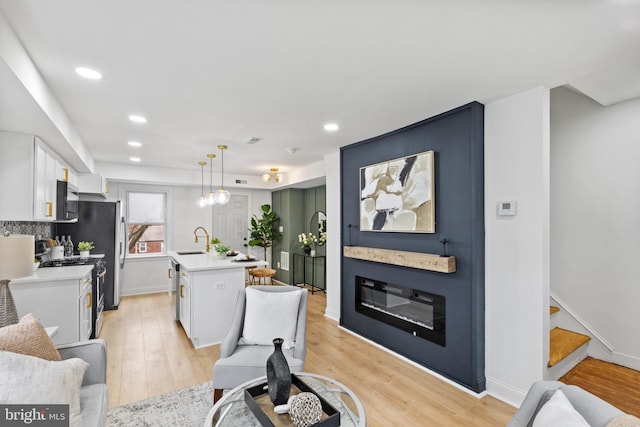 interior space with sink, decorative light fixtures, light hardwood / wood-style floors, white cabinetry, and an island with sink