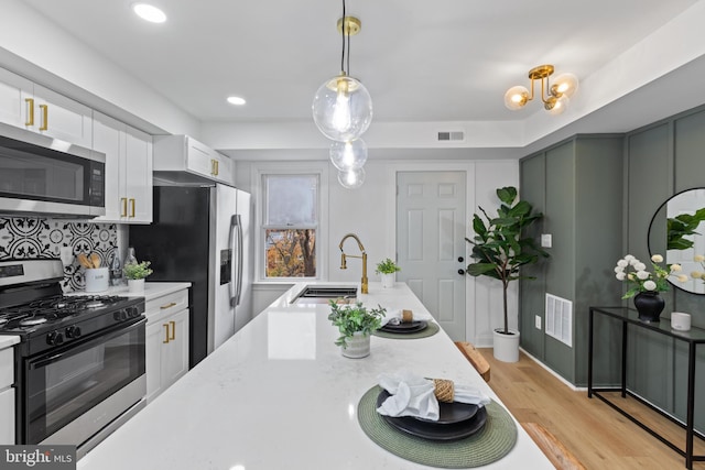 kitchen with white cabinetry, sink, decorative light fixtures, appliances with stainless steel finishes, and light wood-type flooring