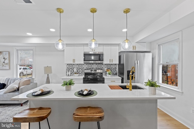 kitchen with decorative backsplash, a breakfast bar, stainless steel appliances, white cabinets, and hanging light fixtures