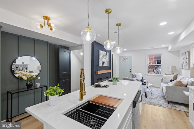 kitchen with white cabinetry, sink, stainless steel dishwasher, light hardwood / wood-style floors, and decorative light fixtures