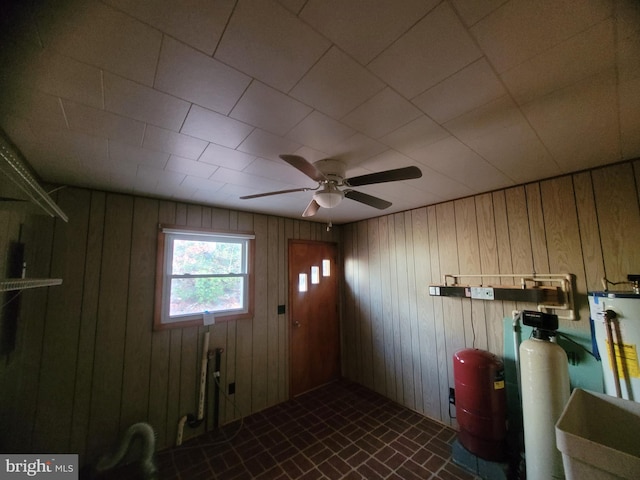 laundry room with gas water heater, ceiling fan, and wood walls