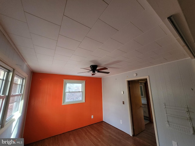 spare room featuring ceiling fan, dark wood-type flooring, and wood walls