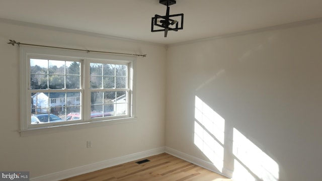 spare room featuring ornamental molding, light wood-style flooring, visible vents, and baseboards