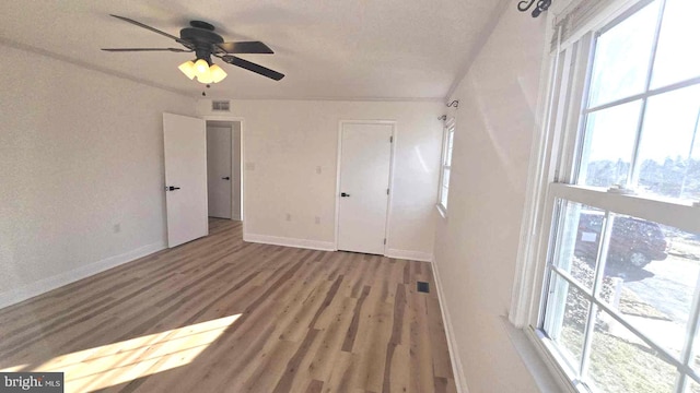 unfurnished bedroom featuring a ceiling fan, visible vents, baseboards, and wood finished floors