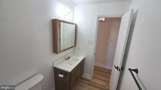 half bath with baseboards, vanity, toilet, and wood finished floors