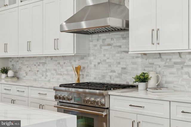 kitchen with high end stainless steel range, extractor fan, tasteful backsplash, light stone counters, and white cabinets