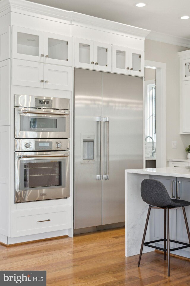 kitchen with appliances with stainless steel finishes, white cabinetry, a kitchen bar, ornamental molding, and light hardwood / wood-style floors