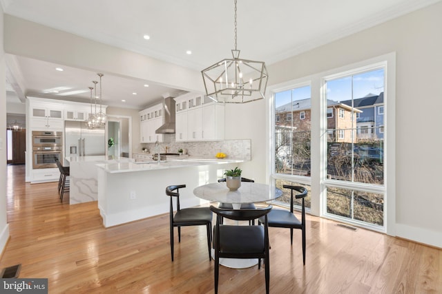 dining room featuring an inviting chandelier, sink, crown molding, and light hardwood / wood-style floors