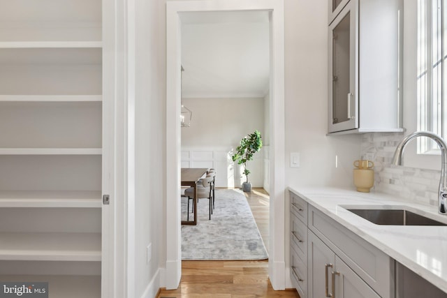 kitchen featuring sink, gray cabinets, light stone counters, light hardwood / wood-style floors, and decorative backsplash