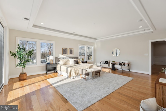 bedroom featuring a tray ceiling, light hardwood / wood-style floors, and multiple windows