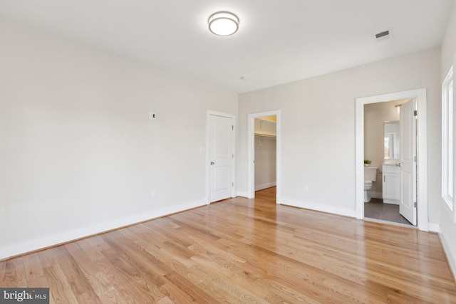 unfurnished bedroom featuring connected bathroom, a spacious closet, light hardwood / wood-style floors, and a closet