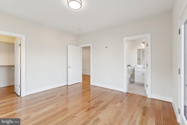 unfurnished bedroom featuring a spacious closet, ensuite bath, light hardwood / wood-style floors, and a closet