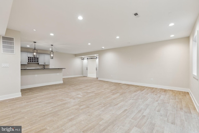 unfurnished living room featuring a barn door and light wood-type flooring