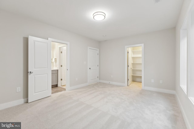 unfurnished bedroom featuring ensuite bathroom, a walk in closet, light colored carpet, and a closet