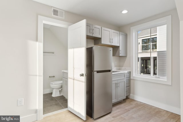 kitchen with gray cabinets, stainless steel refrigerator, and light hardwood / wood-style floors