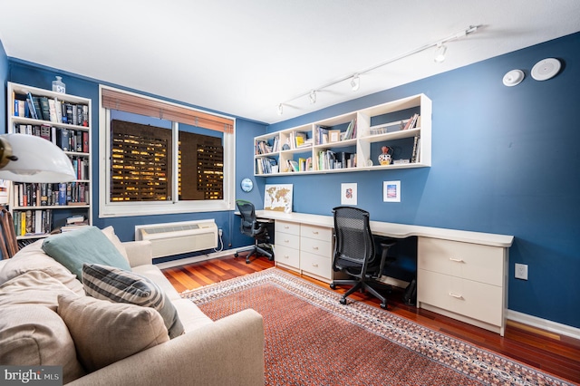 office featuring rail lighting, built in desk, dark wood-type flooring, and a wall unit AC