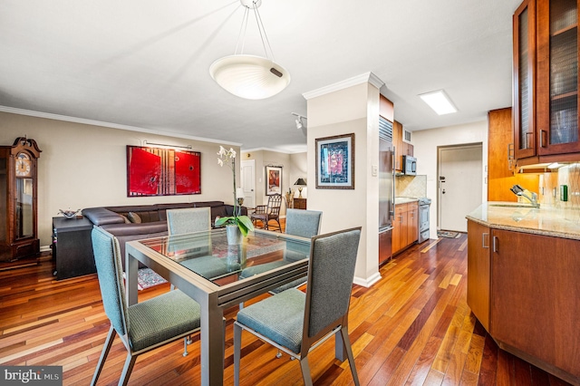 dining room with sink, wood-type flooring, and crown molding