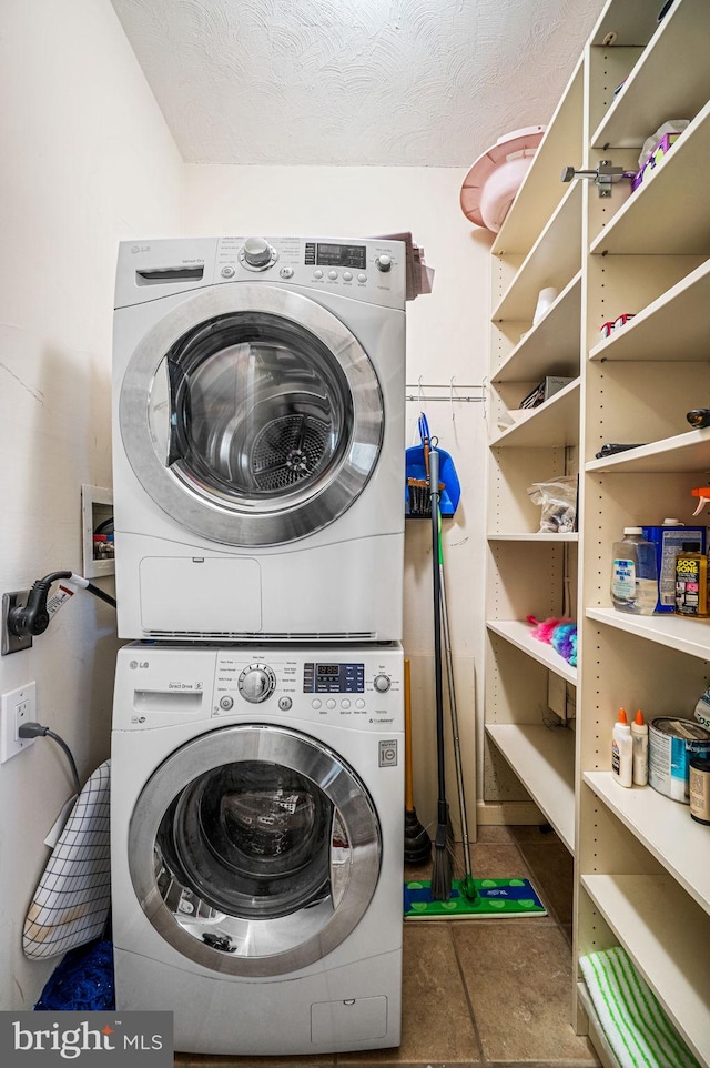 laundry area featuring dark tile patterned floors, stacked washing maching and dryer, and a textured ceiling