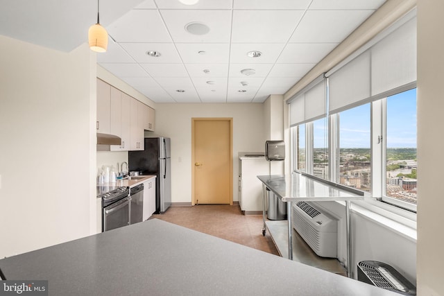 kitchen featuring a drop ceiling, white cabinets, an AC wall unit, decorative light fixtures, and stainless steel appliances