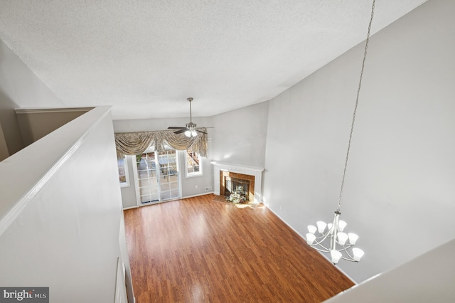 unfurnished living room with a textured ceiling, ceiling fan with notable chandelier, wood-type flooring, and a tile fireplace