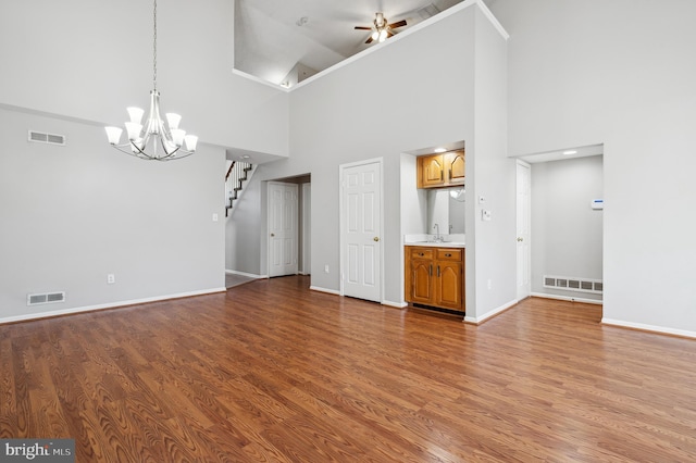 unfurnished living room with ceiling fan with notable chandelier, a high ceiling, and hardwood / wood-style flooring