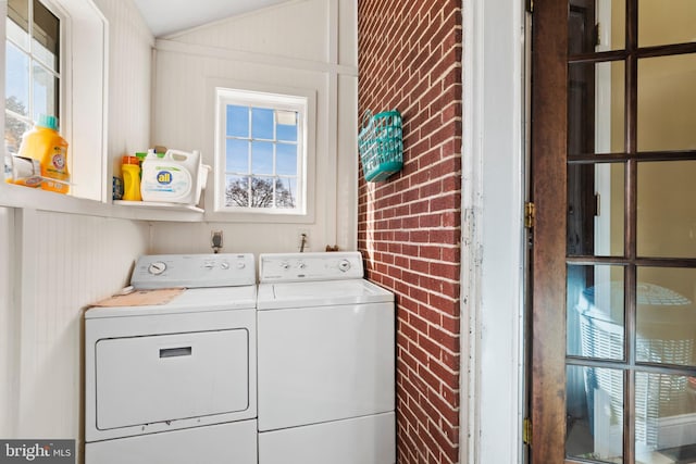 laundry area featuring separate washer and dryer, a healthy amount of sunlight, and brick wall