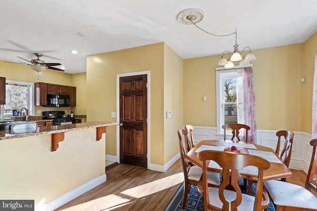 dining room featuring ceiling fan with notable chandelier, sink, and dark wood-type flooring