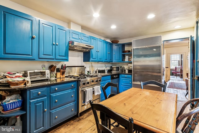 kitchen featuring premium appliances, light hardwood / wood-style floors, dark stone countertops, and blue cabinetry