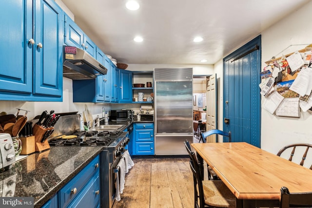 kitchen featuring dark stone counters, premium appliances, sink, blue cabinetry, and light hardwood / wood-style flooring