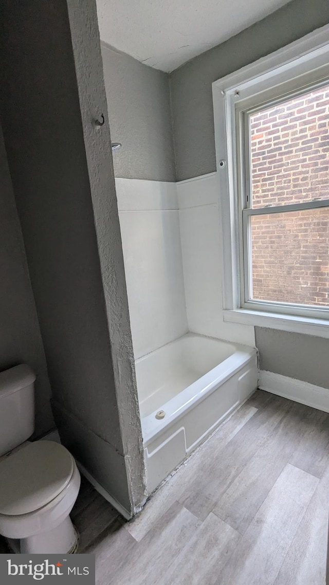 bathroom featuring a washtub, hardwood / wood-style floors, and toilet