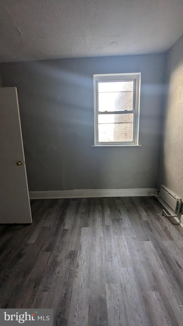 unfurnished room featuring hardwood / wood-style floors, a baseboard radiator, and a textured ceiling