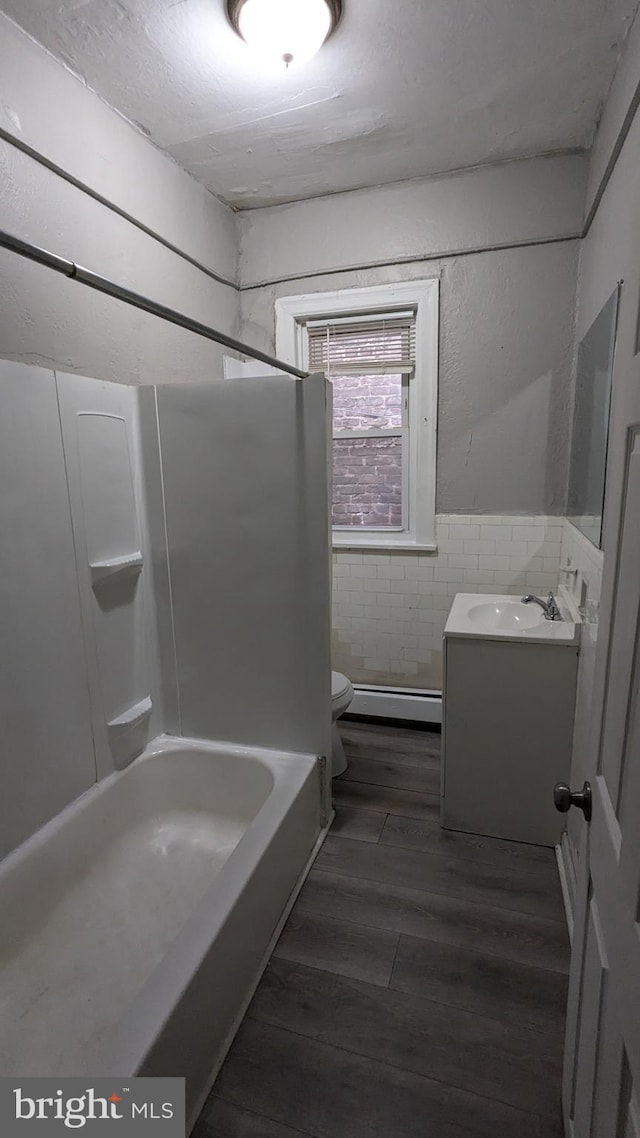 bathroom with vanity, a baseboard heating unit, wood-type flooring, tile walls, and toilet