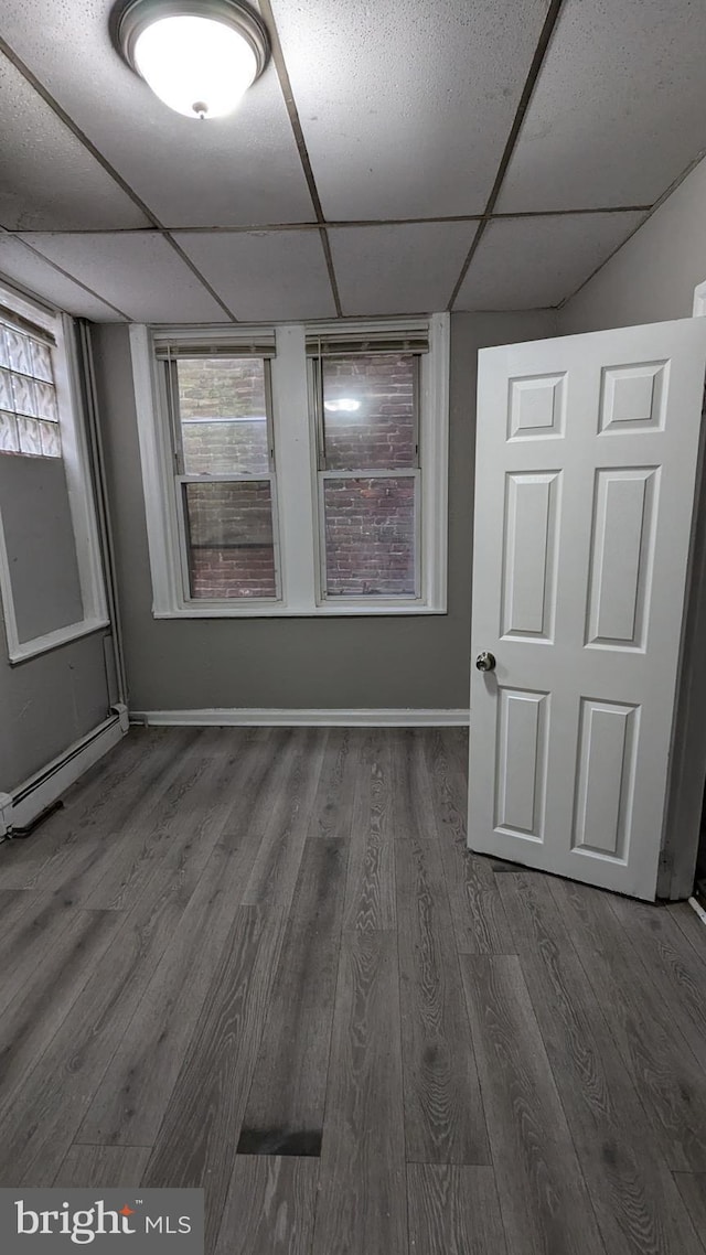 unfurnished room featuring a drop ceiling, dark hardwood / wood-style floors, and a baseboard radiator