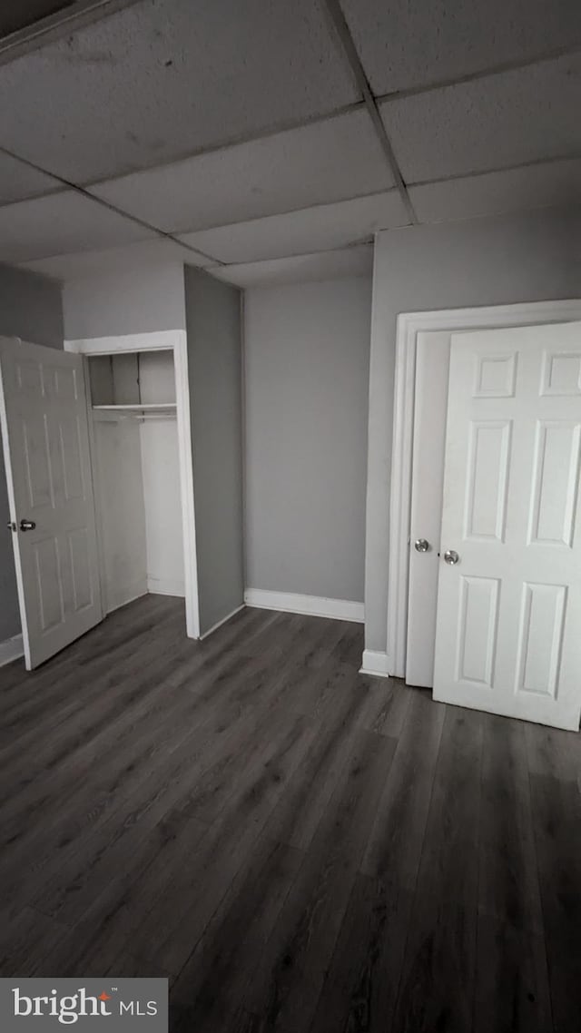 unfurnished bedroom featuring a closet, dark hardwood / wood-style floors, and a drop ceiling