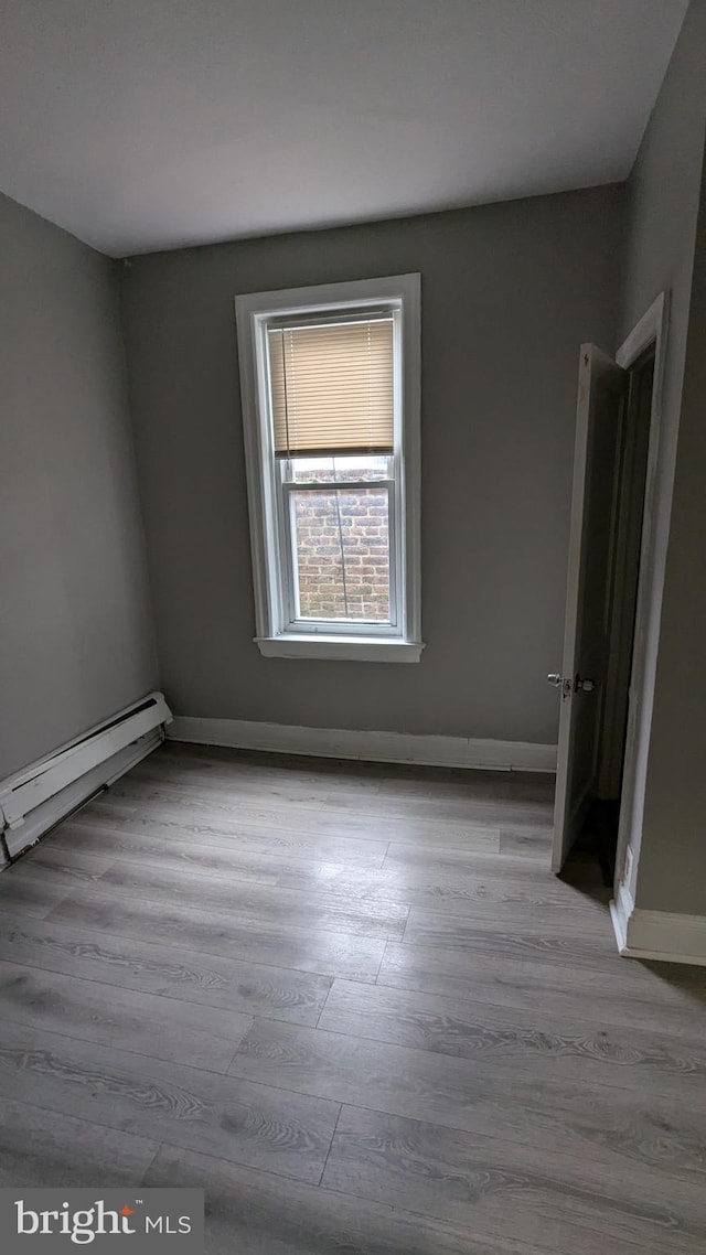 spare room featuring baseboard heating and light hardwood / wood-style floors