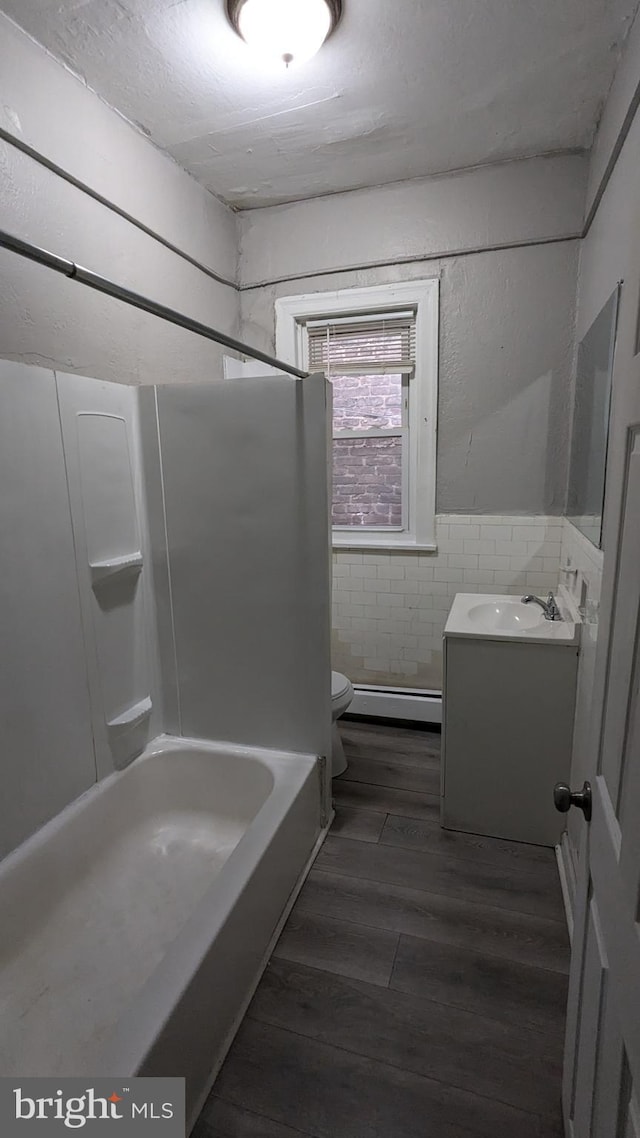 bathroom with vanity, toilet, baseboard heating, tile walls, and wood-type flooring