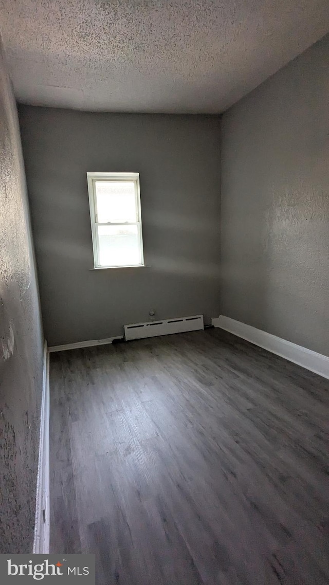 empty room with baseboard heating, a textured ceiling, and dark hardwood / wood-style floors