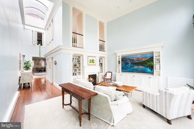 living room with a high ceiling, built in features, ornamental molding, and wood-type flooring