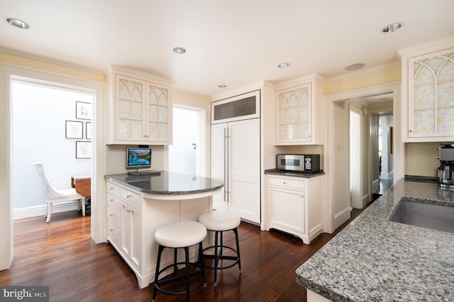 kitchen with a kitchen breakfast bar, dark stone countertops, dark wood-type flooring, and ornamental molding