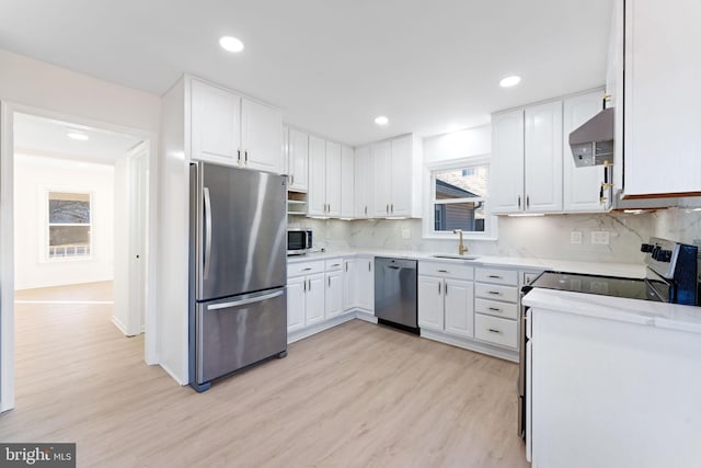 kitchen with backsplash, white cabinets, sink, light wood-type flooring, and appliances with stainless steel finishes