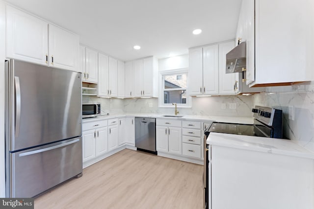 kitchen with light hardwood / wood-style floors, white cabinetry, range hood, and appliances with stainless steel finishes