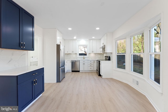 kitchen with white cabinets, blue cabinets, light hardwood / wood-style flooring, decorative backsplash, and stainless steel appliances