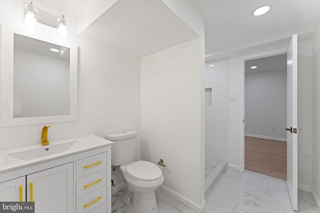 bathroom featuring a tile shower, vanity, and toilet