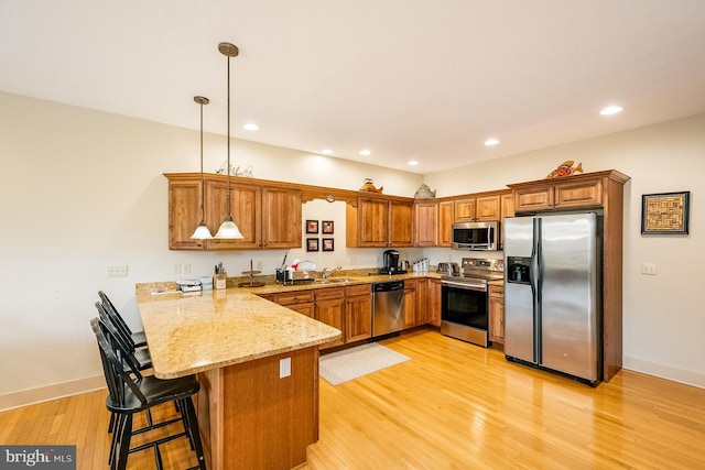 kitchen featuring kitchen peninsula, a breakfast bar, stainless steel appliances, light hardwood / wood-style floors, and hanging light fixtures