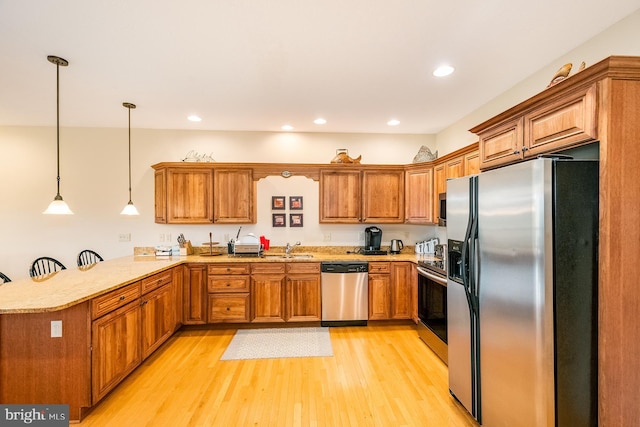 kitchen featuring hanging light fixtures, kitchen peninsula, light hardwood / wood-style floors, a kitchen bar, and appliances with stainless steel finishes